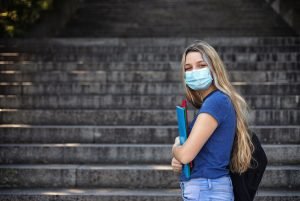 Student girl holding books while walking in school. She wears a mask for COVID-19, Coronavirus protection. Back to school concept